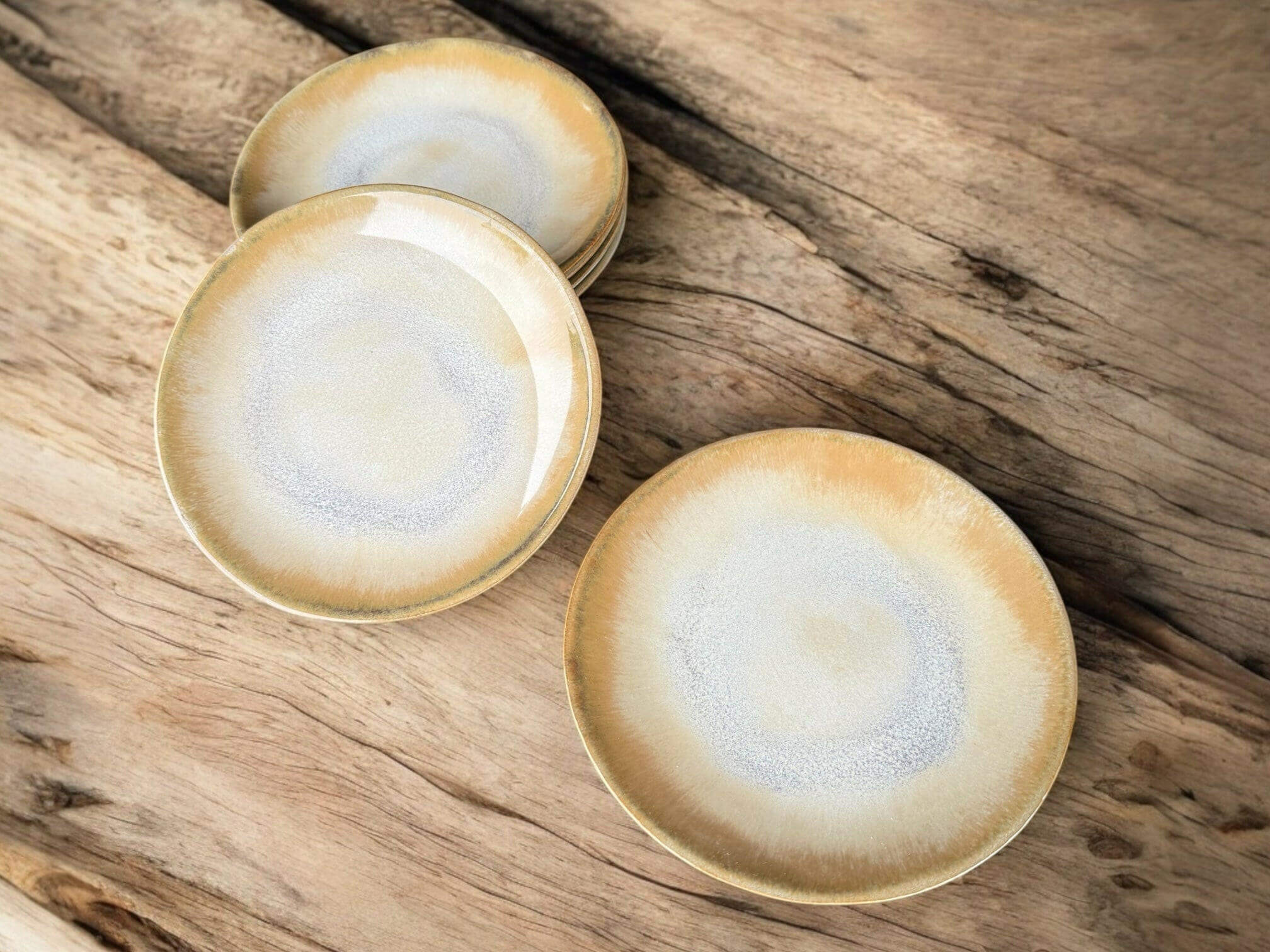 Handmade ceramic plates with creamy beige and grey-blue tones, resting on a rustic wooden surface.