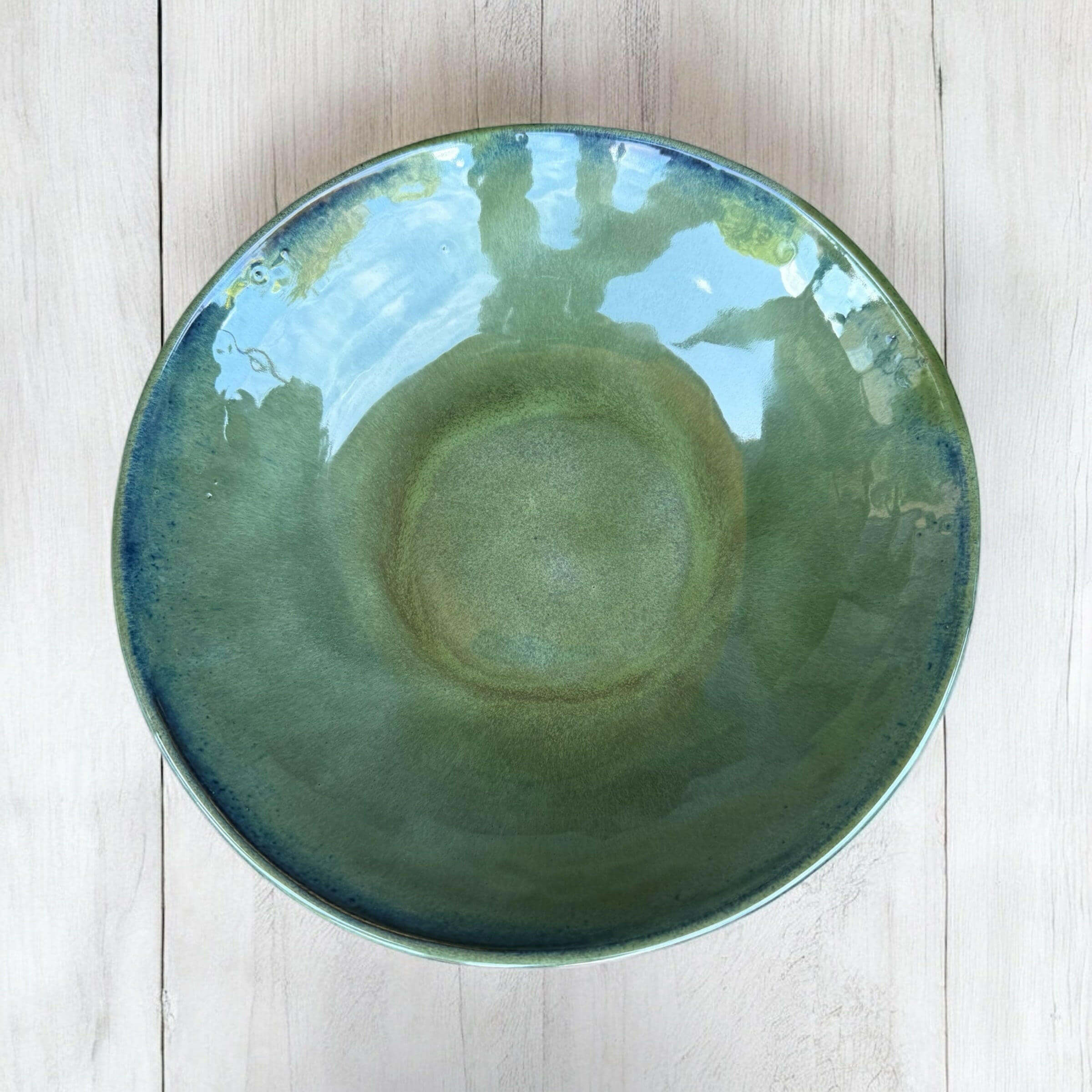 Handmade ceramic bowl in rich green tones with a deep blue rim, featuring a glossy finish.