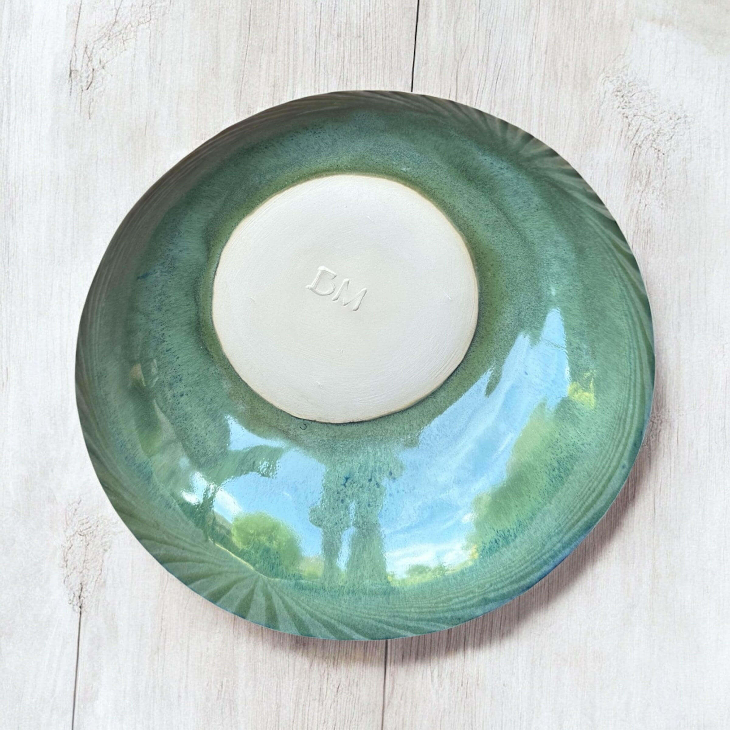Handmade ceramic bowl with rich green tones and blue rim, showcasing unique glazing from above.