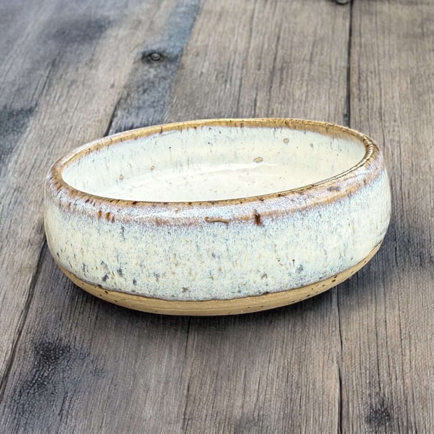Handmade ceramic cat bowl with a soft glaze, featuring a shallow design and natural tones on a wooden surface.