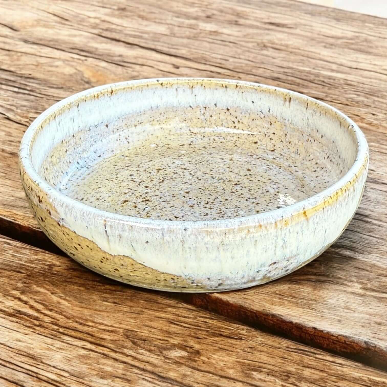 Handmade ceramic cat bowl with soft speckled glaze in warm beige tones on wooden surface.
