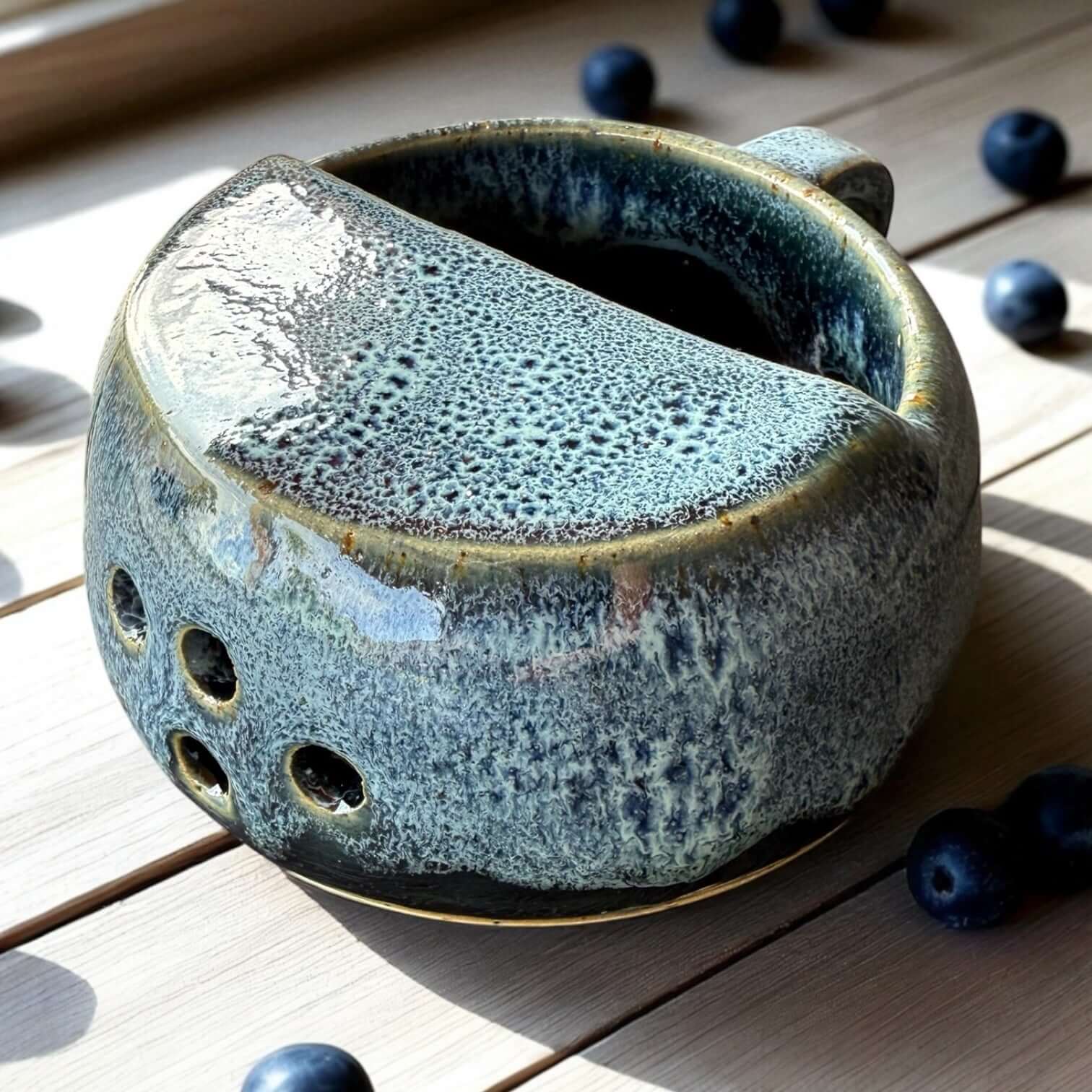 Handmade ceramic berry rinsing mug with blue crater glaze and drainage holes, designed for rinsing berries.