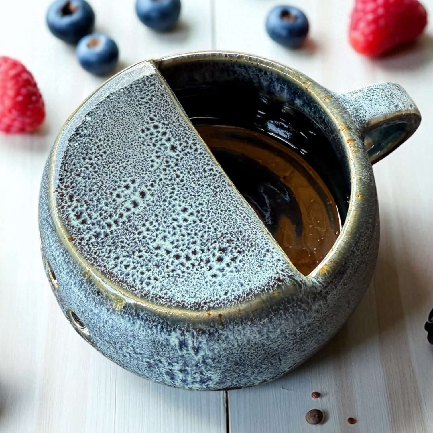 Handmade ceramic berry rinsing mug in glossy blue crater glaze with built-in drainage holes and handle.