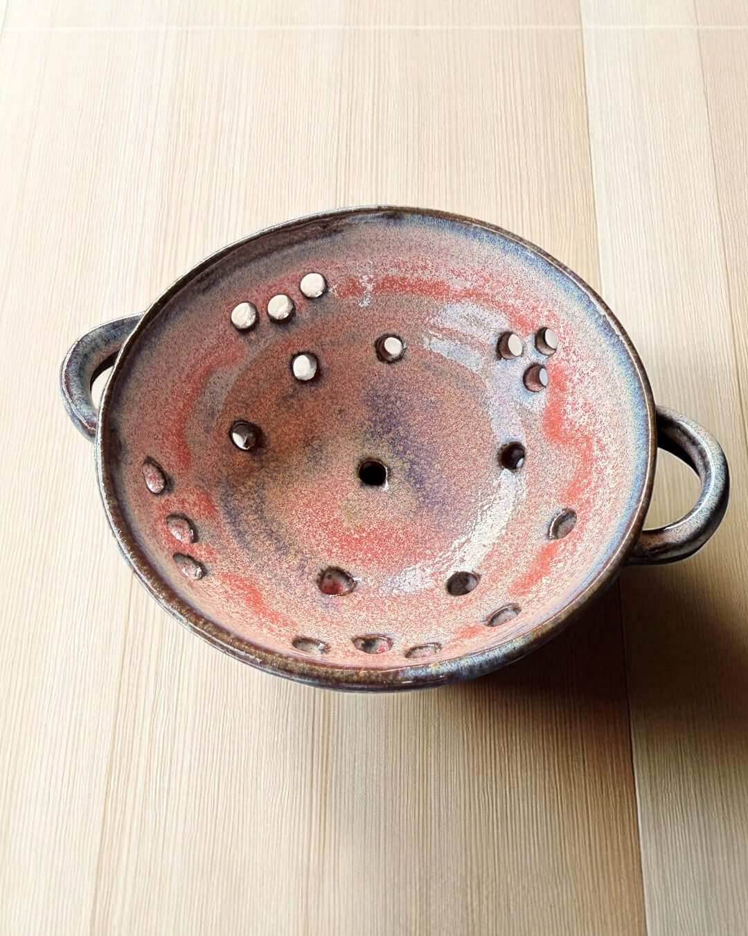 Handmade ceramic berry bowl with pink-white glaze on black clay, ideal for rinsing and serving fresh berries.