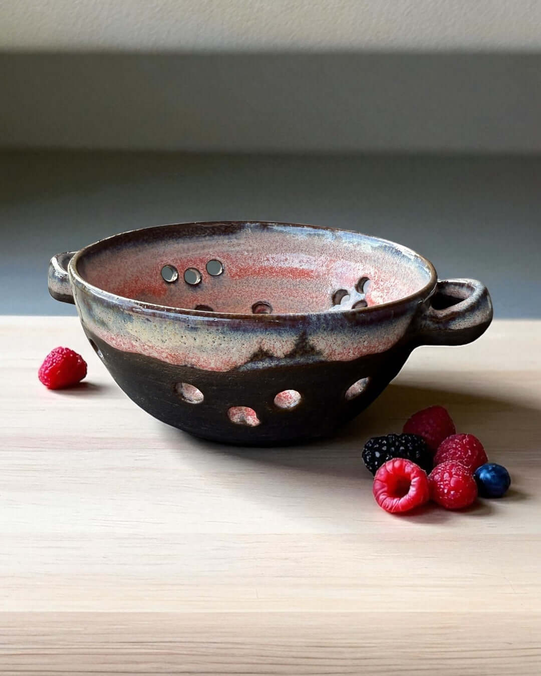 Handmade ceramic berry bowl in pink-white glaze on black clay, perfect for rinsing and serving fresh berries.