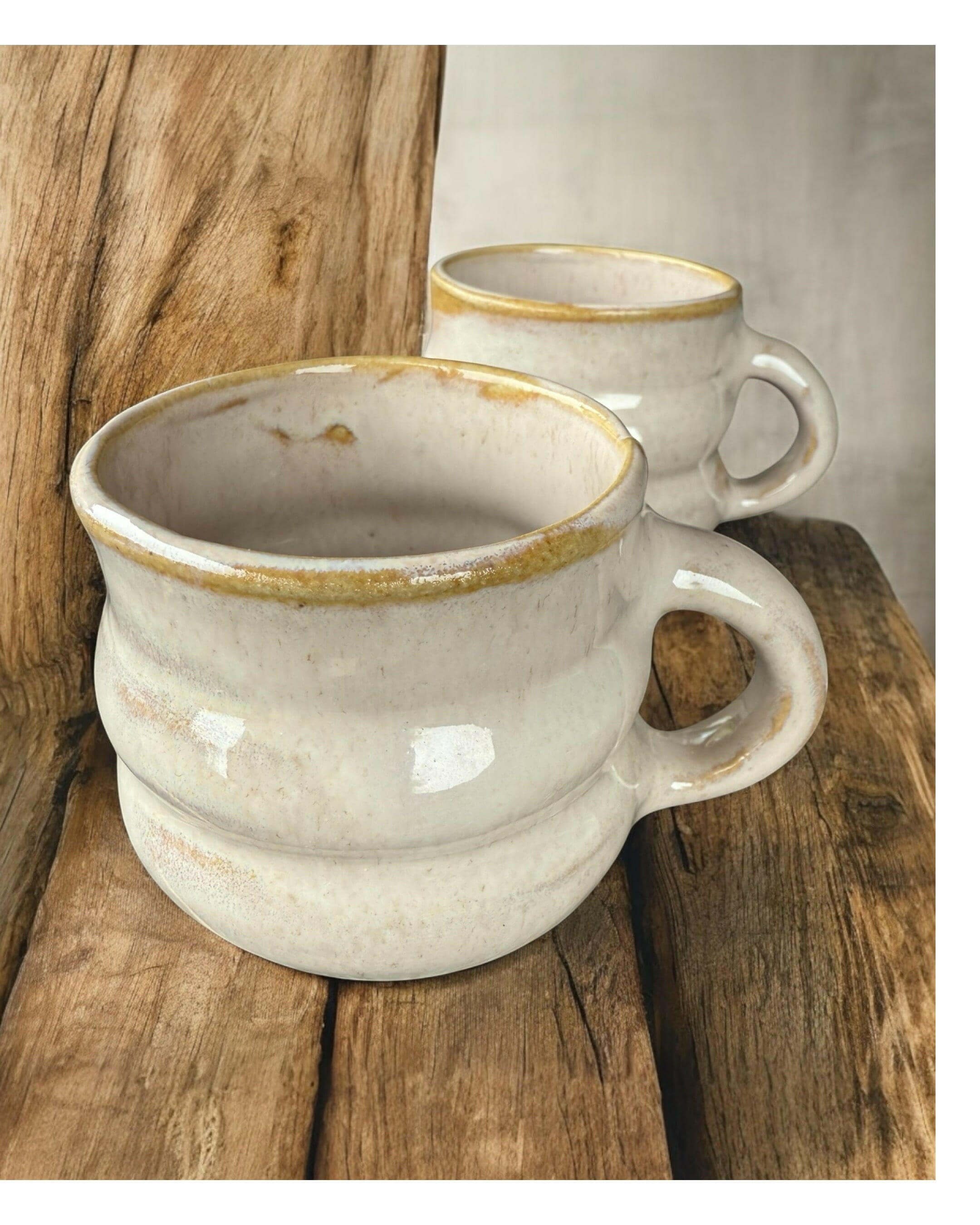 Handmade ribbed speckled stoneware mugs with glossy white glaze and earthy rim, displayed on rustic wooden surface.