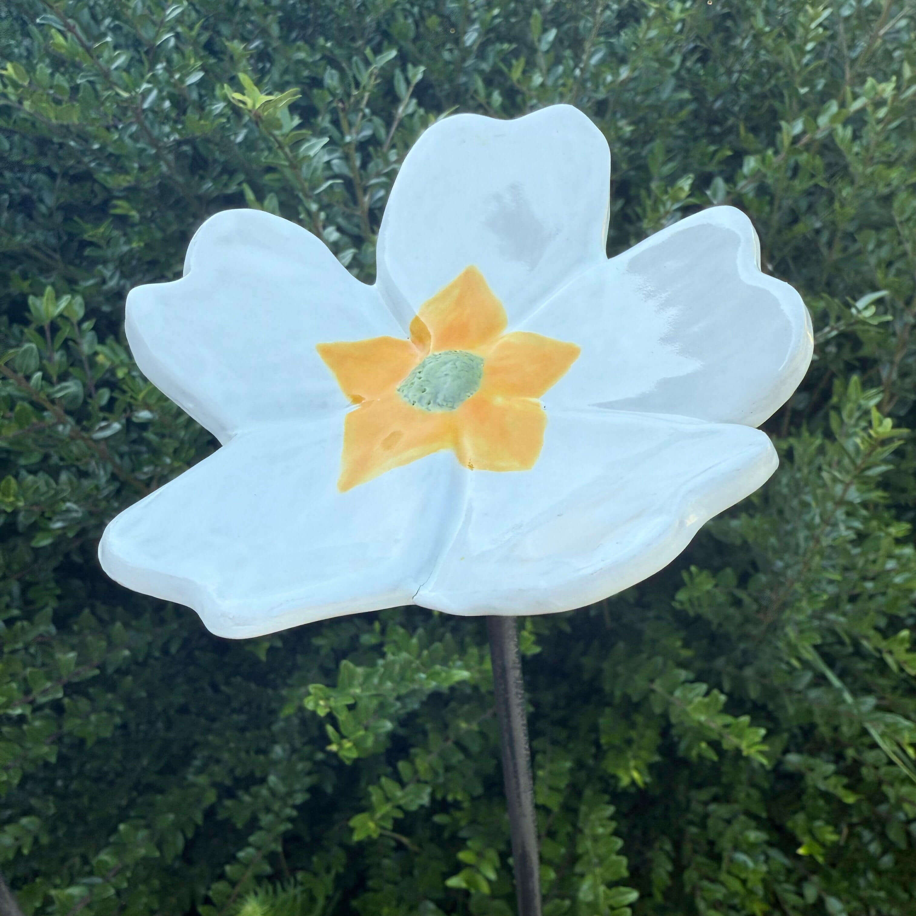 Handmade ceramic garden flower with white petals and yellow center mounted on a stake for outdoor decoration.
