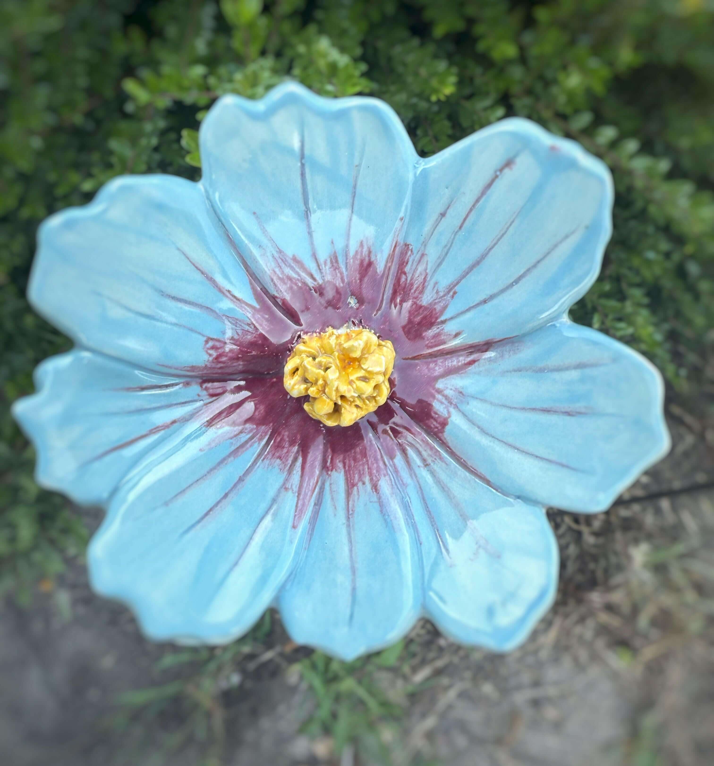 Handmade ceramic garden flower in blue with purple accents and yellow center, perfect for outdoor decor.