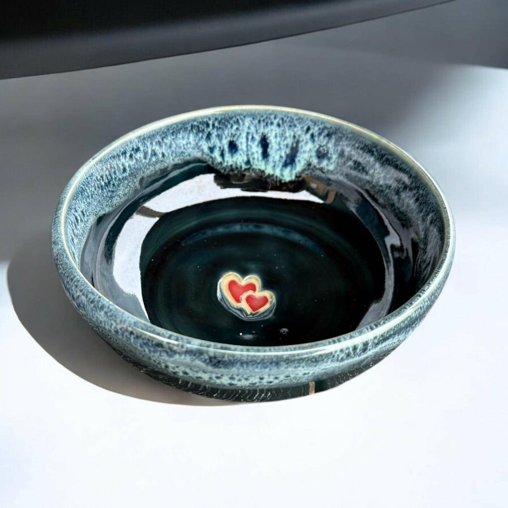 Handmade ceramic bowl with deep blue-green glaze and red heart detail in the center.