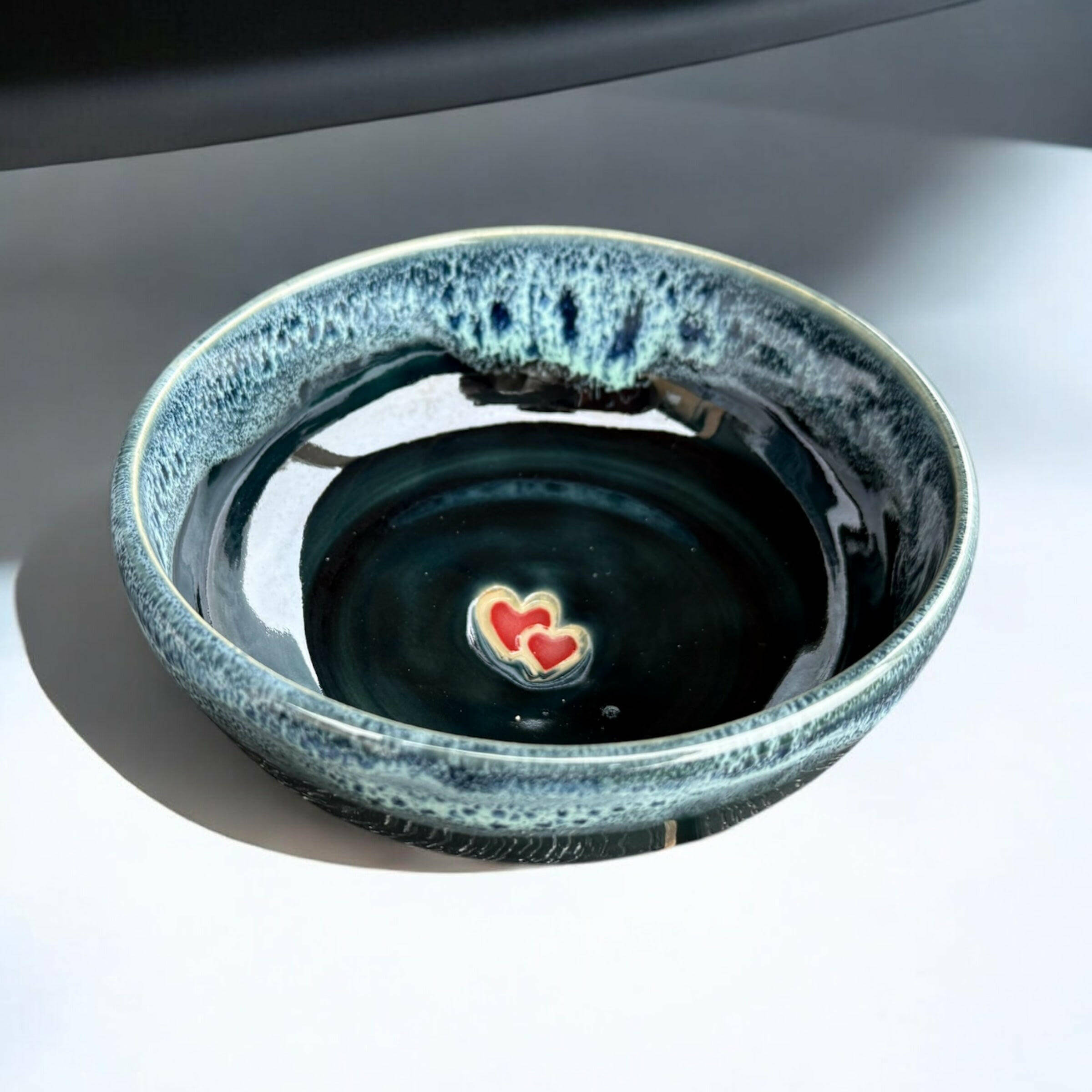 Handmade ceramic bowl with deep blue-green glaze and red heart detail in the center.
