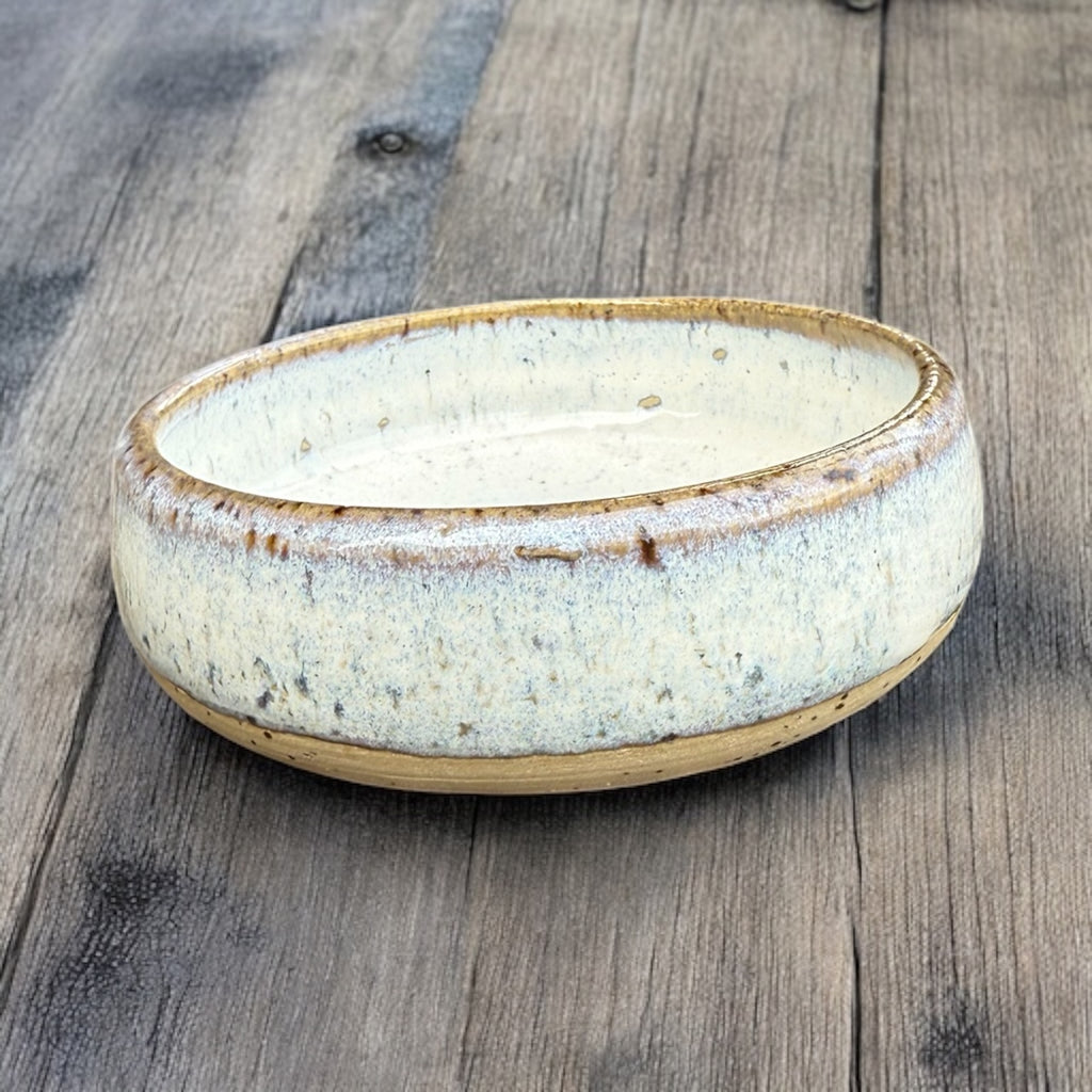 Handmade ceramic cat bowl with a soft glaze, featuring a shallow design and natural tones on a wooden surface.
