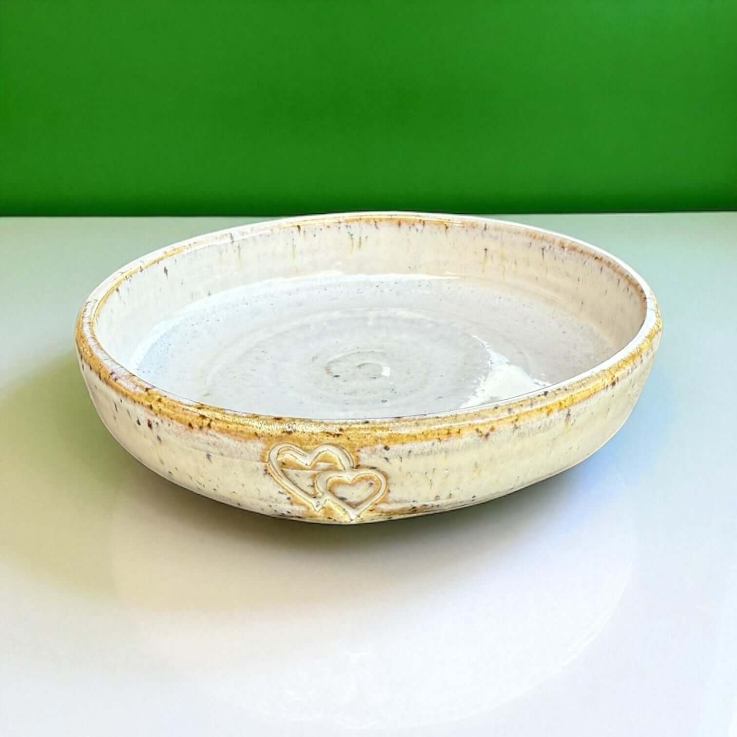 Handmade ceramic cat bowl with hearts, 12 cm diameter, featuring a soft speckled glaze and two embossed hearts.