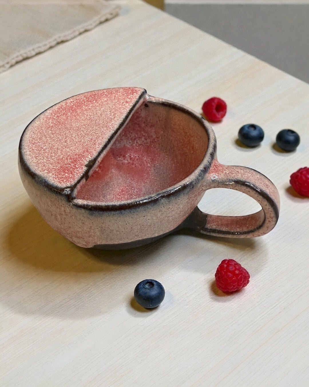 Handmade ceramic berry rinsing mug in soft strawberry glaze with raspberries and blueberries.